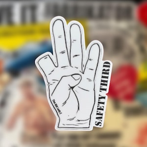 May include: A white sticker with a black outline of a hand showing four fingers extended, with the thumb tucked in. The text "SAFETY THIRD" is printed vertically in black along the right side, and "The Old Lady Z" is printed near the wrist.