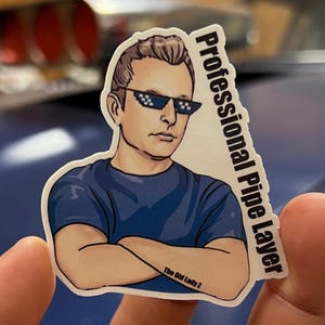 May include: A white sticker with a cartoon illustration of a person wearing sunglasses and a blue shirt with the text "Professional Pipe Layer" and "The Old Lady 2" on it.