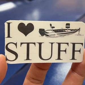 May include: White sticker with black text that reads "I love stuff" with a black heart and a black and white illustration of a boat with the text "The Old Lady I" on it.
