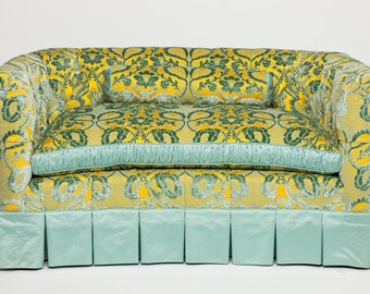 May include: A yellow and green patterned sofa with a light blue skirt and two matching pillows. The sofa has a tufted back and a rolled arm.