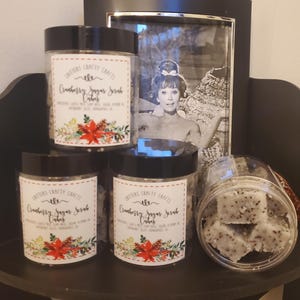 May include: Three glass jars with black lids containing cranberry sugar scrub cubes. The jars have labels that say "Critters Crafty Crafts Cranberry Sugar Scrub Cubes".