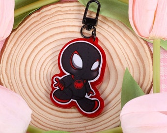 May include: Black and red cartoon character keychain with a black metal ring. The keychain is sitting on a wooden circle surrounded by pink and yellow tulips.