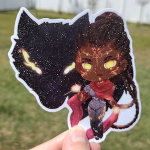 May include: A sticker featuring a cartoon character with dark skin, braided hair, and a red cape. The character is holding a glowing orb in each hand. The character is standing in front of a black wolf with glowing eyes.