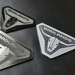 May include: Three black and silver triangular metal emblems with a bull skull and the word "BADLANDS" in white lettering.