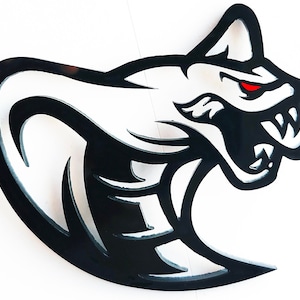 Könnte beinhalten: Schwarze und weiße Wandkunst aus Metall, die eine Kobra mit rotem Auge darstellt. Die Kobra befindet sich in einer angreifenden Pose mit offenem Maul und sichtbaren Zähnen.