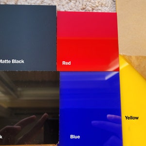 Op de afbeelding: Een verzameling gekleurde acrylplaten in matzwart, rood, zwart, blauw en geel. De matzwarte plaat is gemarkeerd met "Matte Black". De rode plaat is gemarkeerd met "Red". De zwarte plaat is gemarkeerd met "Black". De blauwe plaat is gemarkeerd met "Blue". De gele plaat is gemarkeerd met "Yellow".