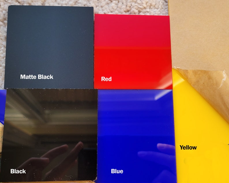 Op de afbeelding: Een verzameling gekleurde acrylplaten in matzwart, rood, zwart, blauw en geel. De matzwarte plaat is gemarkeerd met "Matte Black". De rode plaat is gemarkeerd met "Red". De zwarte plaat is gemarkeerd met "Black". De blauwe plaat is gemarkeerd met "Blue". De gele plaat is gemarkeerd met "Yellow".