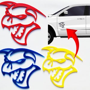 May include: Three car decals in red, blue, and yellow. Each decal features a stylized cartoon of a snarling, toothy creature with a menacing expression. The decals are perfect for adding a touch of personality to any vehicle.
