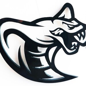 May include: A black metal cobra head silhouette with an open mouth and fangs. The snake's head is in profile, with a curved body. The design is cut out, creating negative space within the shape. The cobra's head is on a white background.