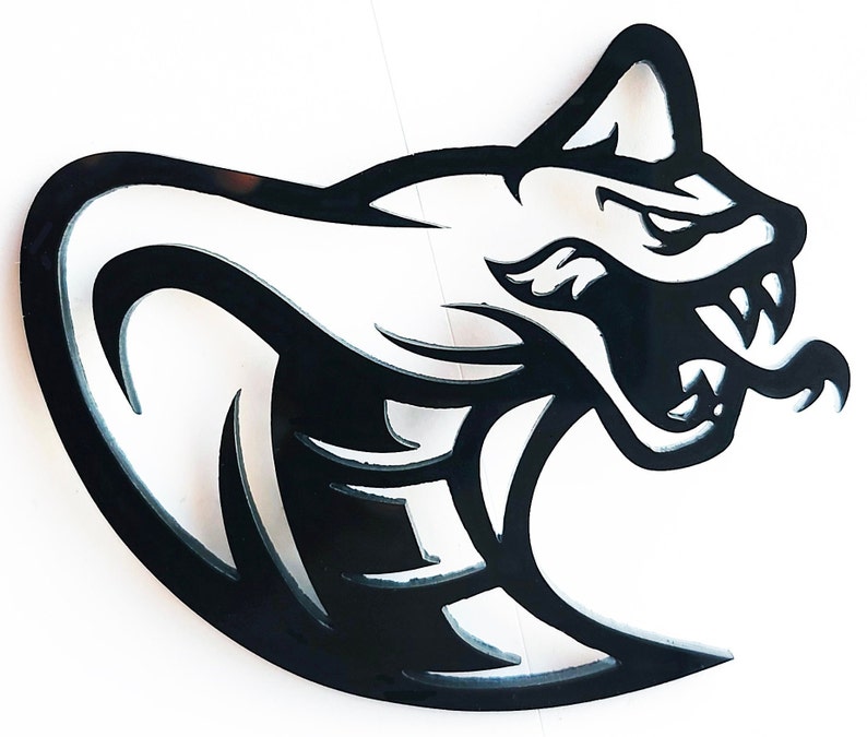 Op de afbeelding: Zwart metalen silhouet van een cobra-kop met een open mond en giftanden. De kop van de slang is in profiel, met een gebogen lichaam. Het ontwerp is uitgesneden, waardoor negatieve ruimte in de vorm ontstaat. De cobra-kop staat op een witte achtergrond.