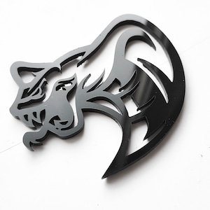 Op de afbeelding: Zwarte decoratieve uitsparing van een gestileerde leeuwenkop en manen. De leeuwenkop is in profiel, met ingewikkelde details in de manen en gelaatstrekken. De uitsparing is gemaakt van massief zwart materiaal.