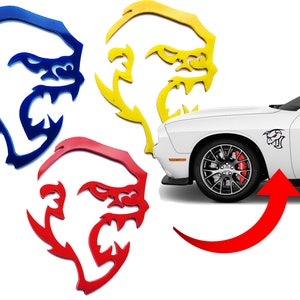 May include: Three car decals in blue, yellow, and red, each featuring a stylized image of a snarling monster. The decals are shown next to a white car with a red brake caliper and a black wheel. The decals are designed to be placed on the side of a car.
