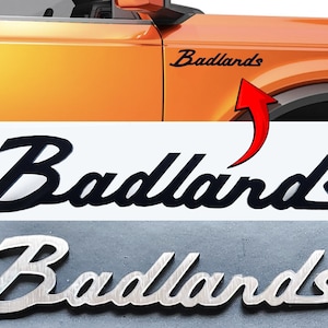 May include: Black and silver "Badlands" emblems. The black emblem is a stylized script font. The silver emblem is a more traditional script font.