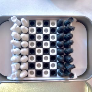 Pode incluir: Uma lata prateada com um design de tabuleiro de xadrez branco e preto. O tabuleiro de xadrez tem quadrados pretos e brancos. H&aacute; pe&ccedil;as de xadrez brancas e pretas no tabuleiro.