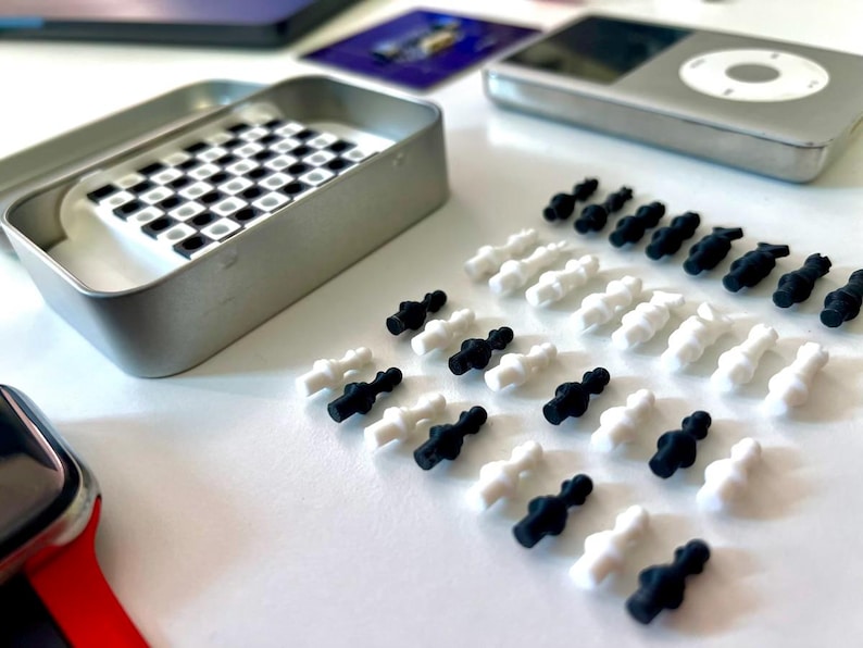 Pode incluir: Um conjunto de pe&ccedil;as de xadrez pretas e brancas sobre uma superf&iacute;cie branca. As pe&ccedil;as s&atilde;o feitas de pl&aacute;stico e t&ecirc;m cerca de 2,5 cm de altura. H&aacute; tamb&eacute;m uma pequena caixa de metal com um tabuleiro de xadrez dentro.