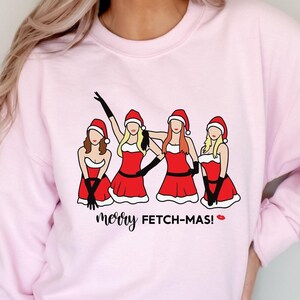 May include: Pink sweatshirt with a graphic of four women dressed as Santa Claus with the text "merry FETCH-MAS!" printed on the front.