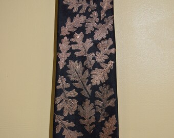 May include: A black silk tie with a white oak leaf design. The leaves are printed in a light brown color. The tie is labeled "White Oak" and "Anne Hanson".