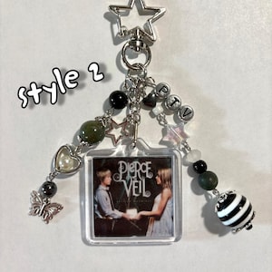 May include: A keychain with a star-shaped clasp and various charms. The charms include beads, a butterfly, a heart, and a small square with a picture of two people and the text "Pierce the Veil". The text "style 2" is also visible.