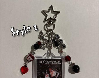 May include: A keychain featuring a square image with the text "MY CHEMICAL ROMANCE" and an image of two people kissing. The keychain has a star-shaped clasp, beads, and charms in red, black, and silver.