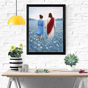 May include: Framed art print depicting two figures walking hand-in-hand through a field of blue flowers. One figure wears a blue dress, the other a white robe with a red sash. The artwork is displayed on a white brick wall.