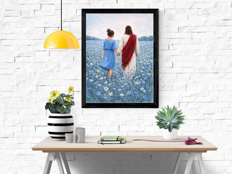 May include: Framed art print depicting two figures walking hand-in-hand through a field of blue flowers. One figure wears a blue dress, the other a white robe with a red sash. The artwork is displayed on a white brick wall.