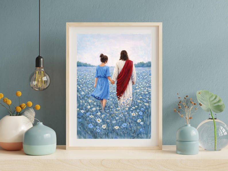 May include: Framed art print depicting two figures walking through a field of blue flowers. One figure wears a blue dress, the other a white robe and red sash. The artwork is displayed on a wooden shelf.