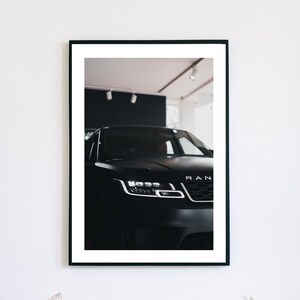 May include: A black Range Rover with the front headlights and grille visible. The car is parked in a showroom with a white ceiling and black walls.