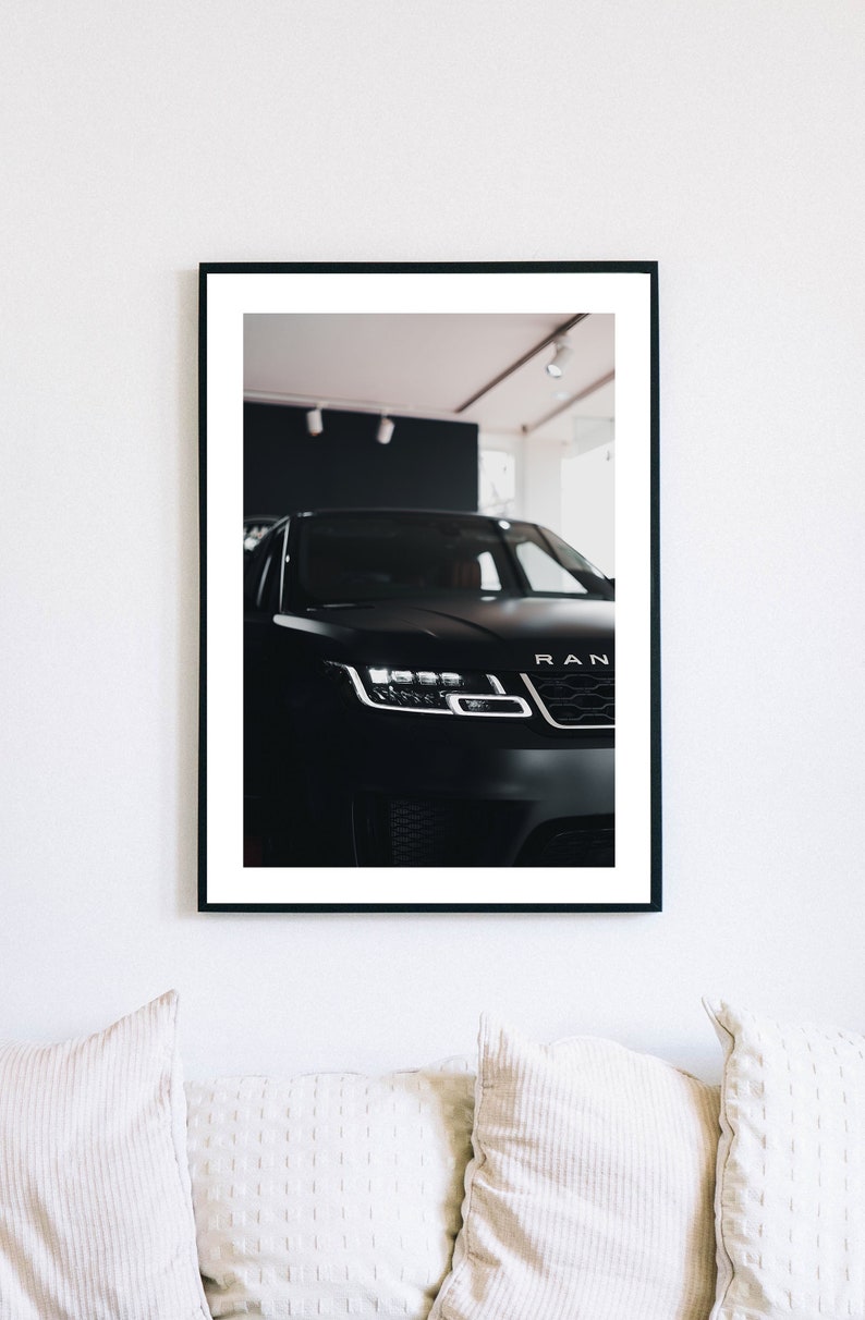 May include: A black Range Rover with the front headlights and grille visible. The car is parked in a showroom with a white ceiling and black walls.