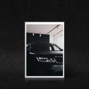 May include: A black SUV with the word "RANGE" visible on the front grill. The car is parked in a showroom with white walls and a white ceiling.