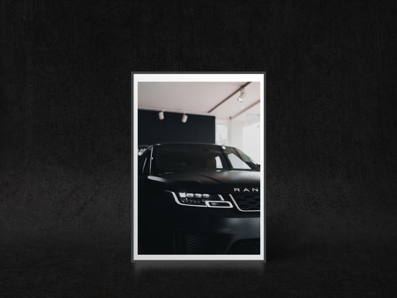 May include: A black SUV with the word "RANGE" visible on the front grill. The car is parked in a showroom with white walls and a white ceiling.