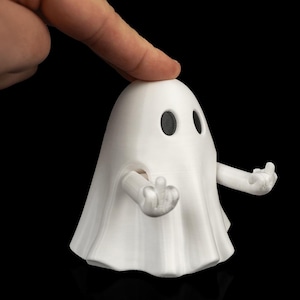 Może przedstawiać: Biała figurka ducha wydrukowana w technologii 3D z gładką, zaokrągloną głową i dwojgiem czarnych, owalnych oczu. Duch ma dwie ruchome ręce wyciągnięte do przodu, a każda dłoń jest uformowana w gest środkowego palca, co nadaje całości humorystyczny wygląd.