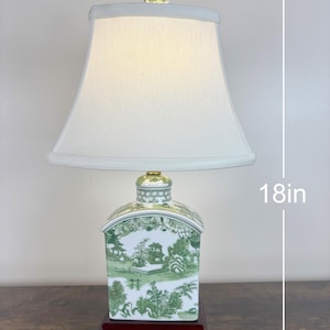 May include: A table lamp, approximately 46 cm tall, with a white lampshade and a ceramic base. The base has a dark red wooden stand and a green and white landscape design. The lamp is topped with a decorative glass orb.