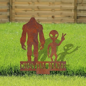 May include: A rusty metal silhouette of Bigfoot and an alien with a peace sign, standing on a base with the text "CUSTOM NAME".