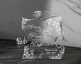 May include: A clear glass puzzle piece with a floral design and the text "Never forget you are the piece that made the difference". The bottom of the piece has the name "Wanda Evans" and the dates "1959-2024".
