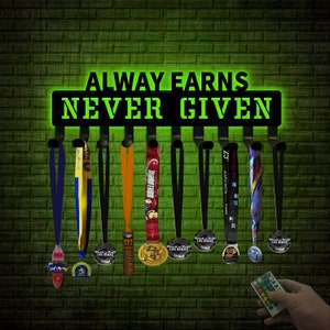 May include: A black metal medal display rack with the words "ALWAYS EARNS NEVER GIVEN" in green neon. Several colorful marathon medals hang from the rack, against a green brick wall.