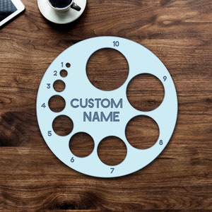 May include: A light blue ring sizer with ten numbered circles. The largest circle has the text "CUSTOM NAME" in the center.