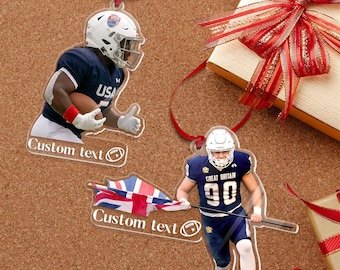 May include: Clear acrylic football player ornaments with red ribbon hangers. One ornament features a player in a USA uniform, the other in a Great Britain uniform. Both have the text "Custom text" and a football graphic.
