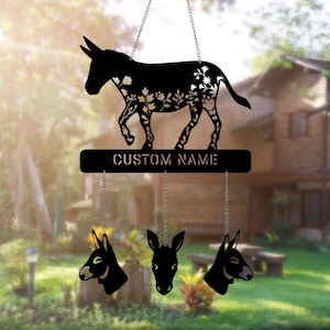May include: Black metal wind chime featuring a donkey silhouette with floral designs. The chime has a sign that reads "CUSTOM NAME" and three smaller donkey head charms hanging below.