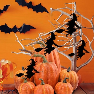 May include: Four black silhouette witches on broomsticks hanging from a branch with orange pumpkins in the foreground.