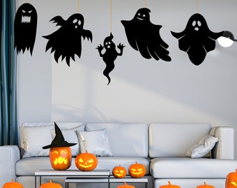 May include: A white couch with black throw pillows sits in front of a wall with six black paper ghost cutouts hanging from the ceiling.  There are nine orange jack-o'-lantern pumpkins on the floor and coffee table in front of the couch.