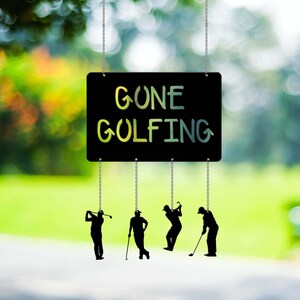 May include: A black sign with the text "Gone Golfing" hanging from chains with five black silhouette figures of golfers swinging golf clubs.
