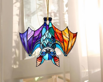 May include: A stained glass bat ornament with a rainbow color scheme. The bat is hanging upside down with its wings spread out. The ornament is made of glass and has a gold string for hanging.