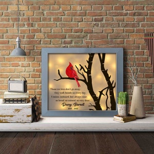 May include: A framed memorial with a red cardinal perched on a branch. The frame has a light grey background and a white mat. The text reads: "Those we love don't go away, they walk beside us every day. Unseen, unheard, but always near, so loved, so missed, so very dear. Dewey Barnett 1949 - 2022"