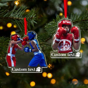 May include: Boxing-themed Christmas ornaments. One ornament features two boxers in red and blue gear, mid-fight. The other shows a boxer in red gear. Both ornaments have a red ribbon for hanging and the text "Custom text".