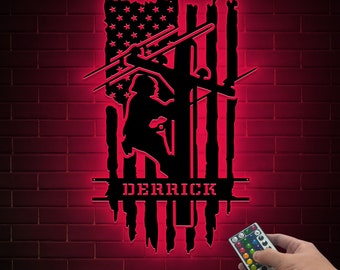 May include: A black metal silhouette of an electrician working on a power line, with the American flag in the background. The name "DERRICK" is written below the silhouette.