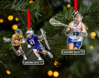 May include: Clear acrylic lacrosse ornaments with red ribbon hangers. The ornaments feature images of lacrosse players in action, with the text "Custom text" at the bottom. One ornament shows a player in a Great Britain uniform.