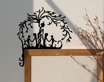 Könnte beinhalten: Schwarze Wanddekoration aus Metall mit einem stilisierten Baum, unter dessen Ästen vier Figuren stehen. Der Baum hat ein fantasievolles, organisches Design mit filigranen Details. Die Figuren sind einfache Silhouetten, die eine Familie oder eine Gruppe von Freunden suggerieren.