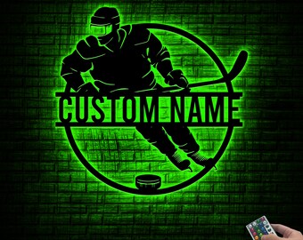 May include: A black silhouette of a hockey player in action, set within a glowing green circle. The words "CUSTOM NAME" are displayed across the center. A hockey puck is at the bottom. The background is a brick wall.