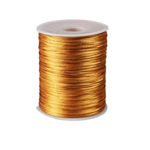 May include: A spool of golden-yellow satin cord. The cord is tightly wound around a white plastic core. The cord has a shiny, smooth texture, and the spool is set against a plain white background. This cord is suitable for various crafting projects.