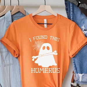 May include: Orange t-shirt with a white ghost holding a bone and the text "I found this humerus".